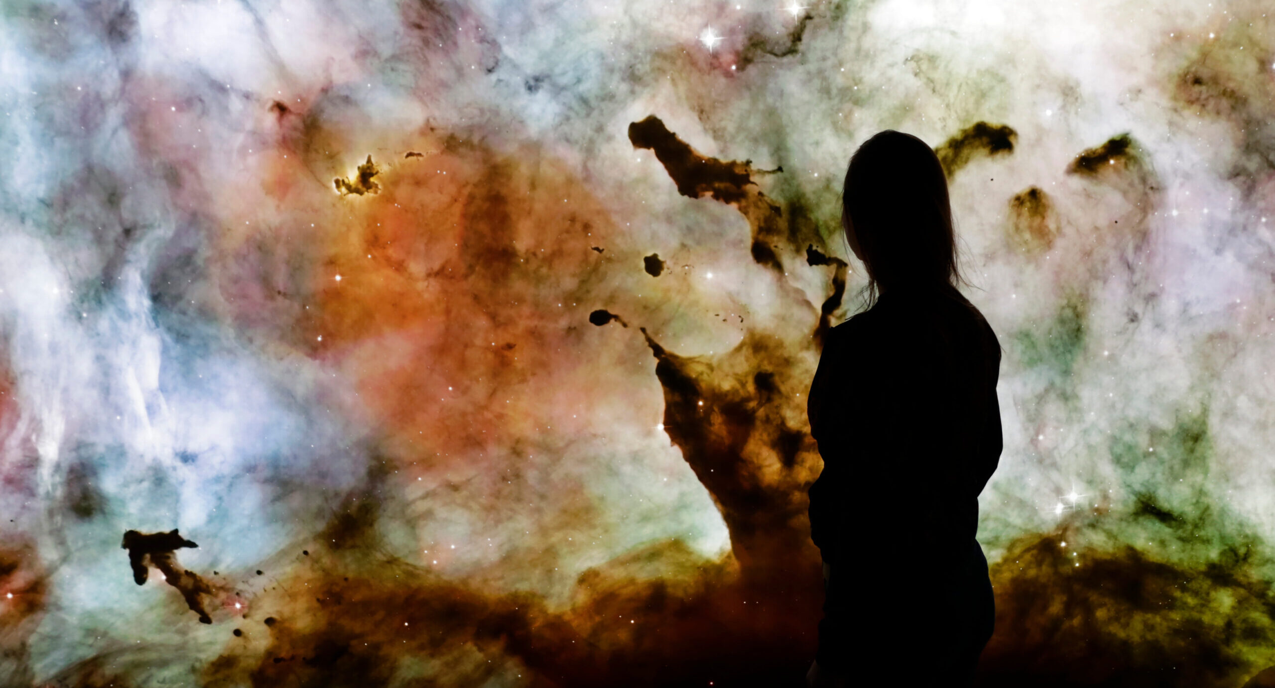 Young woman standing in front of the huge picture of star nebula. Woman in the universe. Woman watching the space. Meaning of life. Visiting the observatory. Elements of the image furnished by NASA.